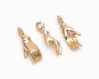 May include: Three gold-colored hand-shaped charms. Each charm is a different pose, with one hand pointing, one open, and one in a relaxed position. The charms are likely for jewelry making or as decorative elements.