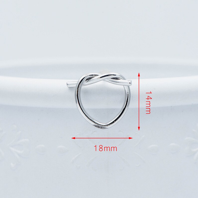 May include: Silver heart-shaped ring with a twisted knot design. The ring measures 18 mm wide and 14 mm high.