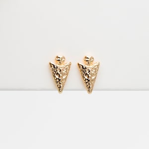 May include: A pair of gold-toned arrowhead stud earrings. The arrowheads have a textured surface.
