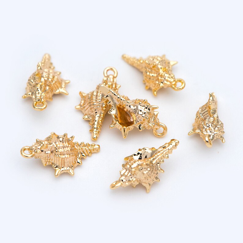 May include: Six gold-colored seashell charms with a textured surface. Each charm has a loop for attaching to jewelry or other crafts.