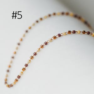 May include: A delicate gold chain necklace with alternating brown and cream colored square beads.