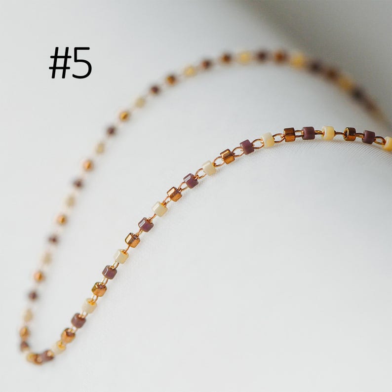 May include: A delicate gold chain necklace with alternating brown and cream colored square beads.