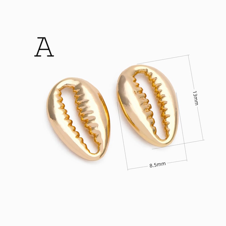 May include: Two gold-colored cowrie shell charms labeled with the letter A. The shells have a smooth, metallic finish and a serrated central opening. Technical lines indicate a length of 13mm and a width of 8.5mm for the shell on the right.