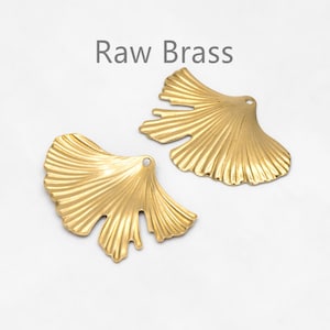 May include: Two gold-colored metal ginkgo leaf charms with a raw brass finish. The leaves have a detailed, textured design.