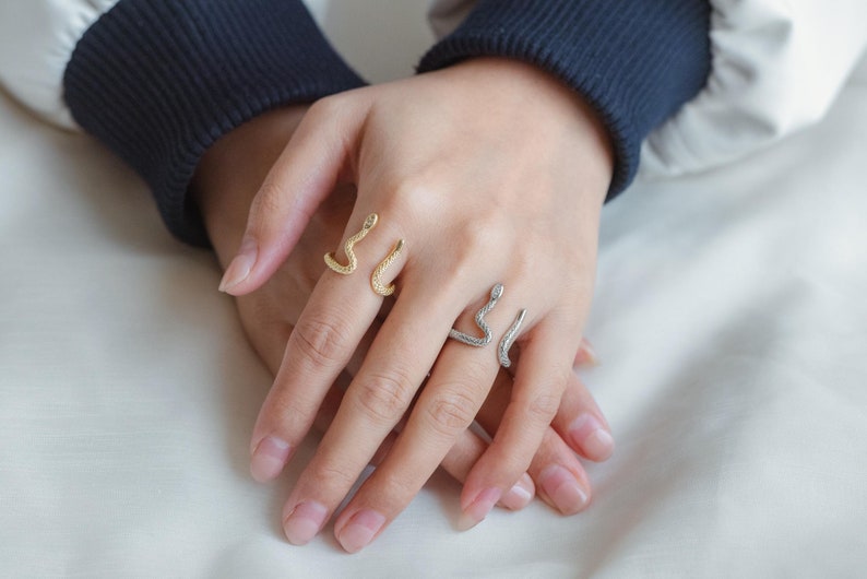 May include: Two snake-shaped rings on a person's fingers. One ring is gold and the other is silver.