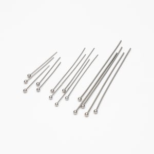 May include: A set of silver head pins with round heads. The pins are arranged in a fan shape on a white background.