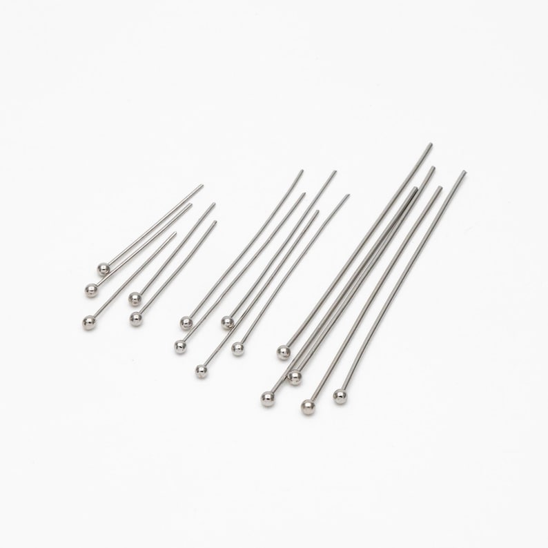 May include: A set of silver head pins with round heads. The pins are arranged in a fan shape on a white background.
