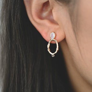 May include: Gold hoop earrings with a clear teardrop-shaped stone at the top. The hoop is textured and has a small drop pendant.
