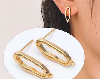 May include: Gold-colored oval stud earrings with a textured surface. The earrings have a post for insertion and a small loop at the bottom. One earring is shown on an ear.