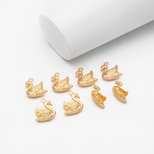 May include: Eight gold swan charms, each with a detailed design, perfect for jewelry making or crafting projects.