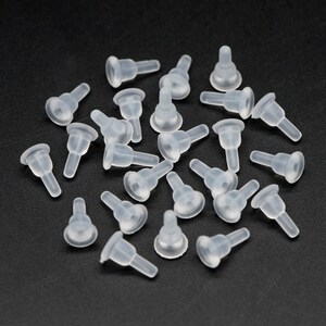 May include: A group of 25 clear plastic bottle stoppers. The stoppers are shaped like a small cone with a wider base. They are all lying on a black surface.