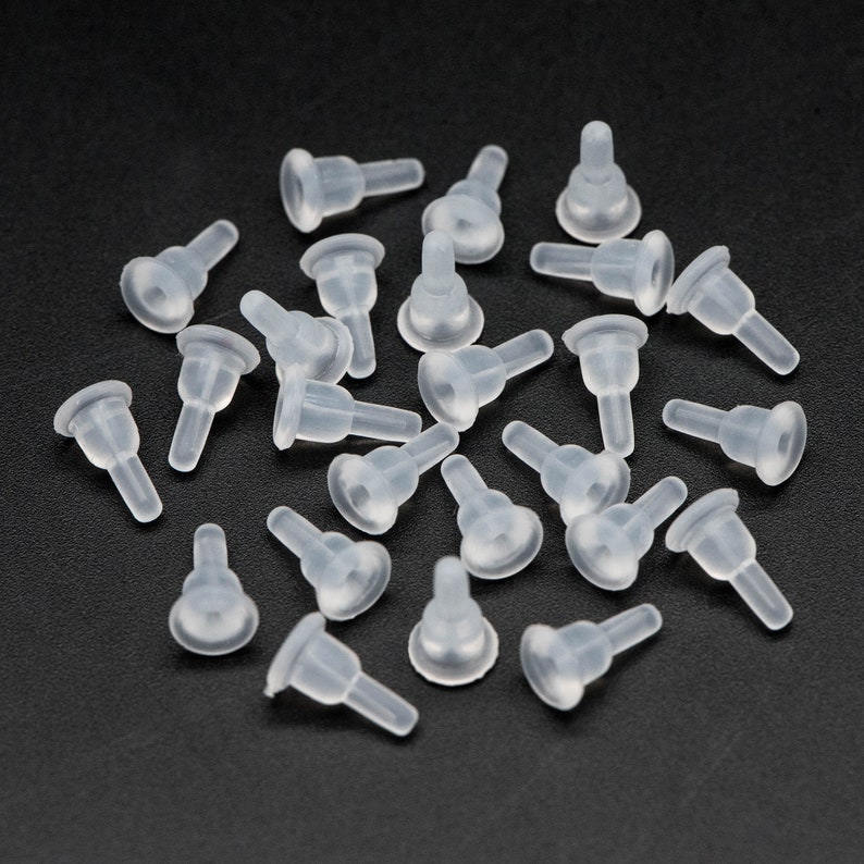 May include: A group of 25 clear plastic bottle stoppers. The stoppers are shaped like a small cone with a wider base. They are all lying on a black surface.