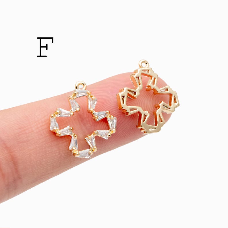 Pu&ograve; includere: Due ciondoli a forma di croce color oro. Un ciondolo &egrave; impreziosito da cristalli rettangolari trasparenti. L'altro ciondolo ha un design geometrico. La lettera "F" &egrave; nell'angolo in alto a sinistra.