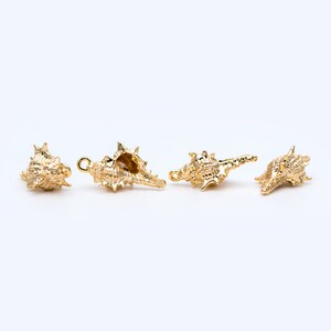 May include: Four gold-colored seashell charms with a detailed, textured surface. The charms have a loop for attaching to jewelry or other crafts.