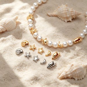 May include: A pearl necklace with gold seashell, starfish, and turtle charms. Additional charms are scattered on a sandy surface, along with seashells. The necklace and charms are in gold and silver tones.