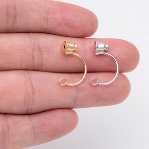May include: Two earring hooks, one gold and one silver, with a small round bead at the top of each hook.