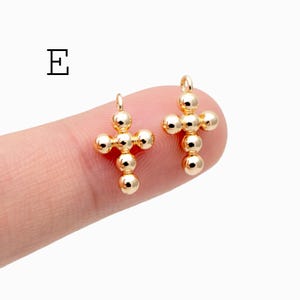 Pu&ograve; includere: Due ciondoli a forma di croce color oro, ciascuno composto da perline sferiche. Le croci hanno un piccolo anello nella parte superiore per il fissaggio ai gioielli. La lettera "E" &egrave; nell'angolo in alto a sinistra.