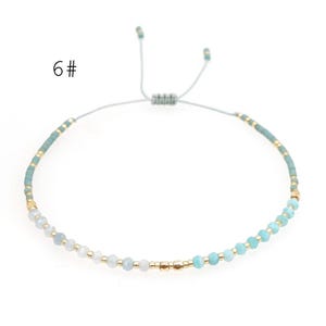 May include: A delicate blue and white beaded bracelet with gold accents. The bracelet is adjustable with a sliding knot.