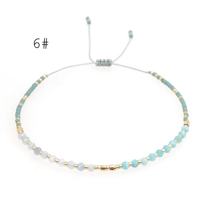 May include: A delicate blue and white beaded bracelet with gold accents. The bracelet is adjustable with a sliding knot.