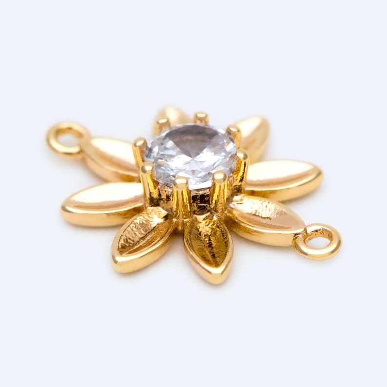 May include: Gold-tone flower charm with a clear rhinestone in the center. The charm has two jump rings for attaching to jewelry.