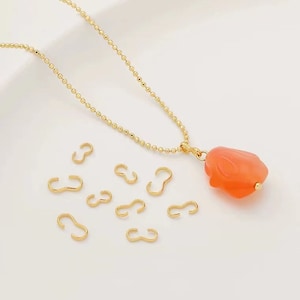 May include: A gold chain necklace with a peach-colored pendant shaped like a rose. The necklace is accompanied by several gold jump rings.