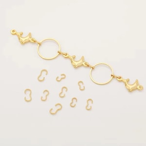 May include: Gold-toned dolphin charms and jump rings for jewelry making. The charms are shaped like dolphins and have a shiny finish. The jump rings are small and round, and are used to connect different parts of jewelry.