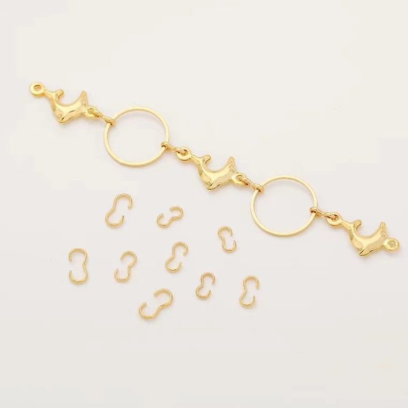 May include: Gold-toned dolphin charms and jump rings for jewelry making. The charms are shaped like dolphins and have a shiny finish. The jump rings are small and round, and are used to connect different parts of jewelry.