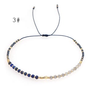 May include: A blue and grey beaded bracelet with a gold accent. The bracelet is adjustable with a sliding knot.