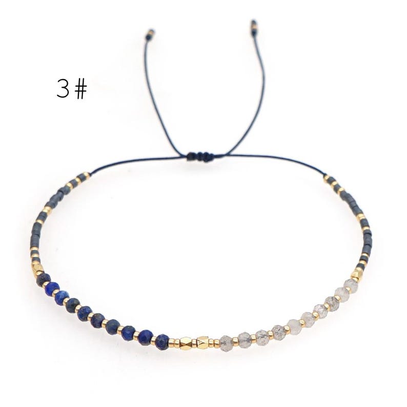 May include: A blue and grey beaded bracelet with a gold accent. The bracelet is adjustable with a sliding knot.
