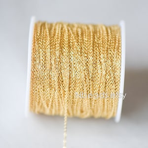 May include: A spool of gold-colored chain, wound around a white plastic spool. The chain is a delicate, fine-link style.
