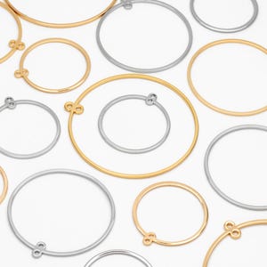 May include: An assortment of gold and silver-colored metal hoop earring components. The hoops vary in size and feature small loops for attaching to earring hooks. The components are arranged on a white background.