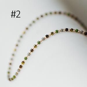 May include: A gold chain necklace with small square beads in shades of green, gray, and black.