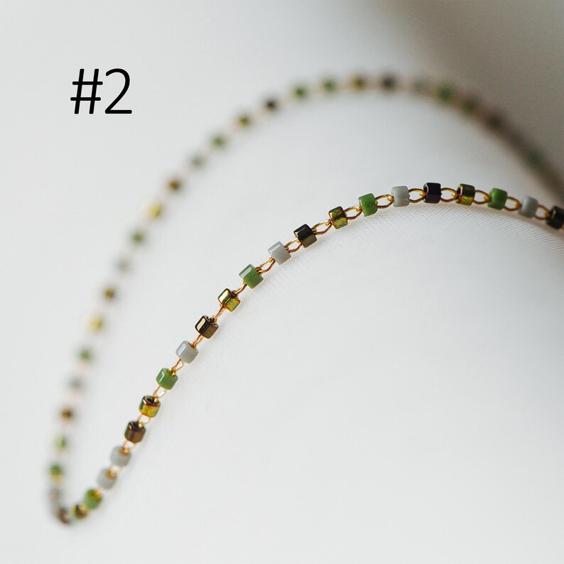 May include: A gold chain necklace with small square beads in shades of green, gray, and black.