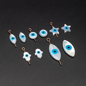 May include: Assortment of white and blue evil eye charms with gold accents. The charms include a star, a hamsa hand, and various eye shapes.