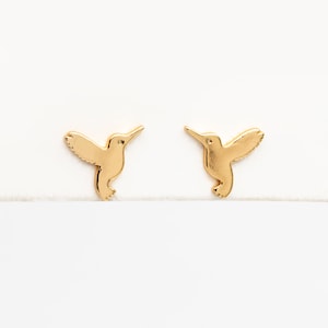 May include: A pair of gold hummingbird stud earrings. The earrings are small and delicate, and they feature a realistic hummingbird design.