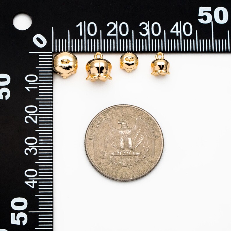 May include: Four gold-colored metal flower charms of varying sizes, measured against a ruler and a US quarter. The charms are in the shape of a bell with a rounded top and a small loop at the top.