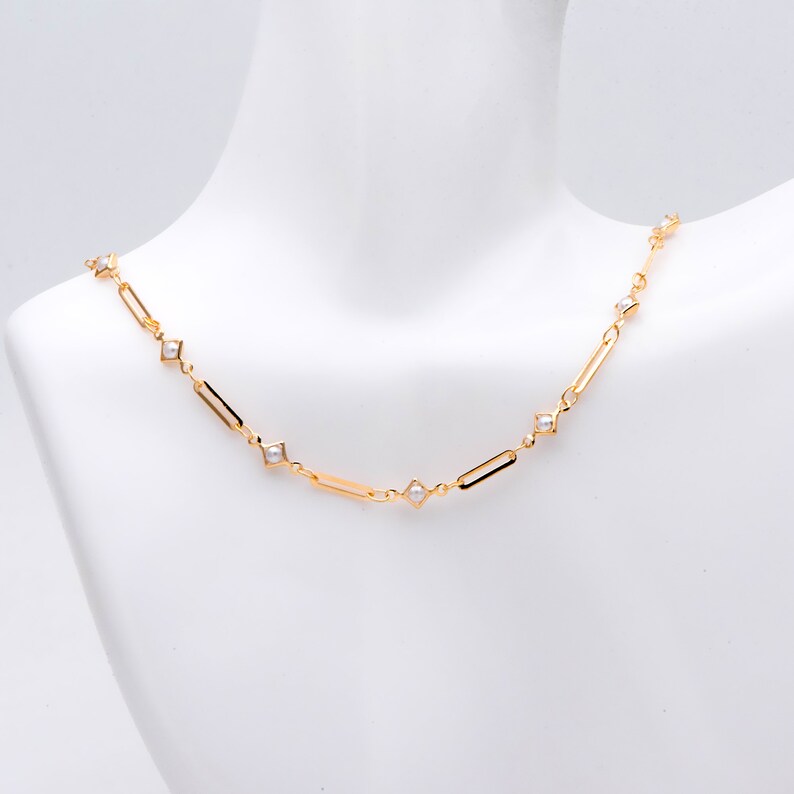 May include: A gold chain necklace with small white pearls set in square-shaped accents.