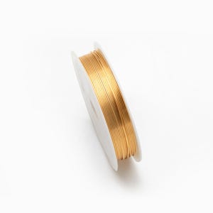 May include: A spool of gold-colored wire on a white plastic bobbin.