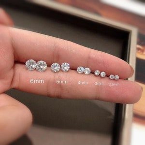 May include: A close-up of a hand holding a set of round, clear, diamond-like earrings in various sizes. The earrings are labeled with their diameter in millimeters: 6mm, 5mm, 4mm, 3mm, and 2.5mm.