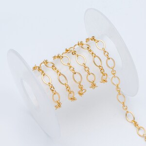 May include: A spool of gold-colored chain with oval links. The chain is wrapped around a white plastic spool.