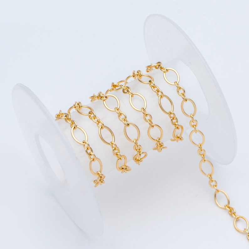 May include: A spool of gold-colored chain with oval links. The chain is wrapped around a white plastic spool.