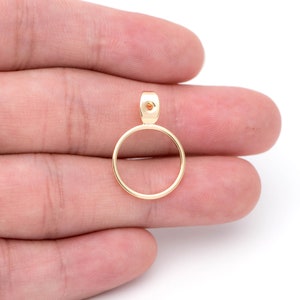 May include: Gold-toned metal pendant with a circular frame and a small hole at the top.