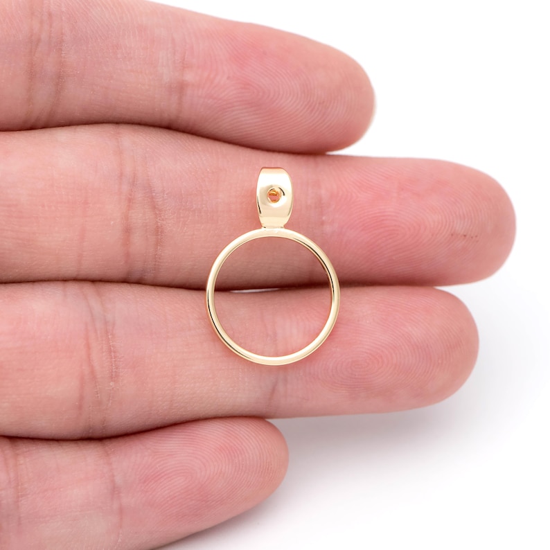 May include: Gold-toned metal pendant with a circular frame and a small hole at the top.