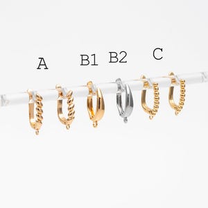 May include: A selection of gold and silver hoop earrings displayed on a clear rod. The earrings have various designs, including textured, braided, and beaded styles. The earrings are labeled A, B1, B2, and C.