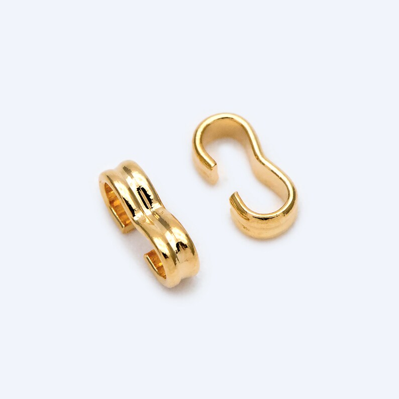 May include: Two gold-toned metal clasps for jewelry making. The clasps are shaped like an 'S' and have a smooth, polished finish.
