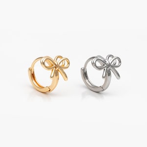 May include: Two hoop earrings with a bow design. The earring on the left is gold and the earring on the right is silver.
