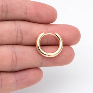 May include: A gold hoop earring with a smooth, polished finish. The earring is held in a hand, showcasing its size and shape.
