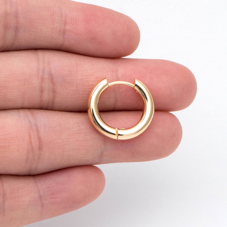 May include: A gold hoop earring with a smooth, polished finish. The earring is held in a hand, showcasing its size and shape.