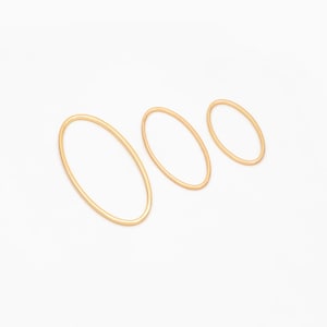 May include: Three gold-colored oval-shaped jewelry findings of varying sizes are arranged on a white background. The findings are thin and have a smooth, polished appearance. The largest oval is on the left, with the other two decreasing in size to the right.