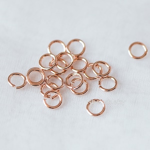 Op de afbeelding: Een stapel roségouden springringen, een soort sieradenbevestiging, op een witte stoffen achtergrond.